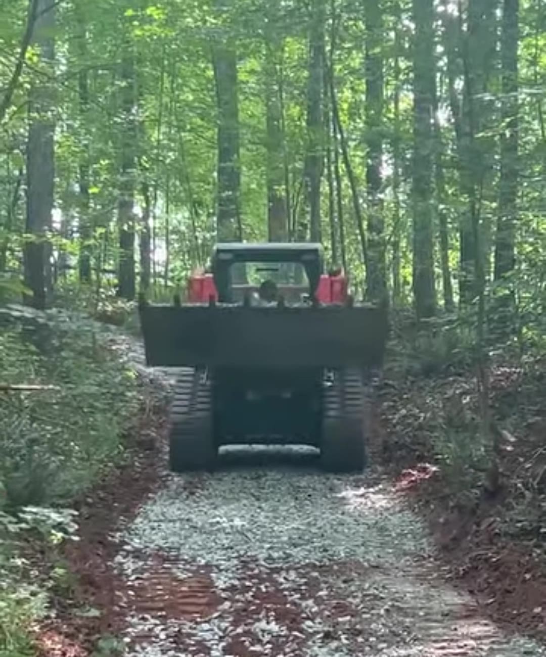 Track loader spreading gravel on a new driveway through the woods