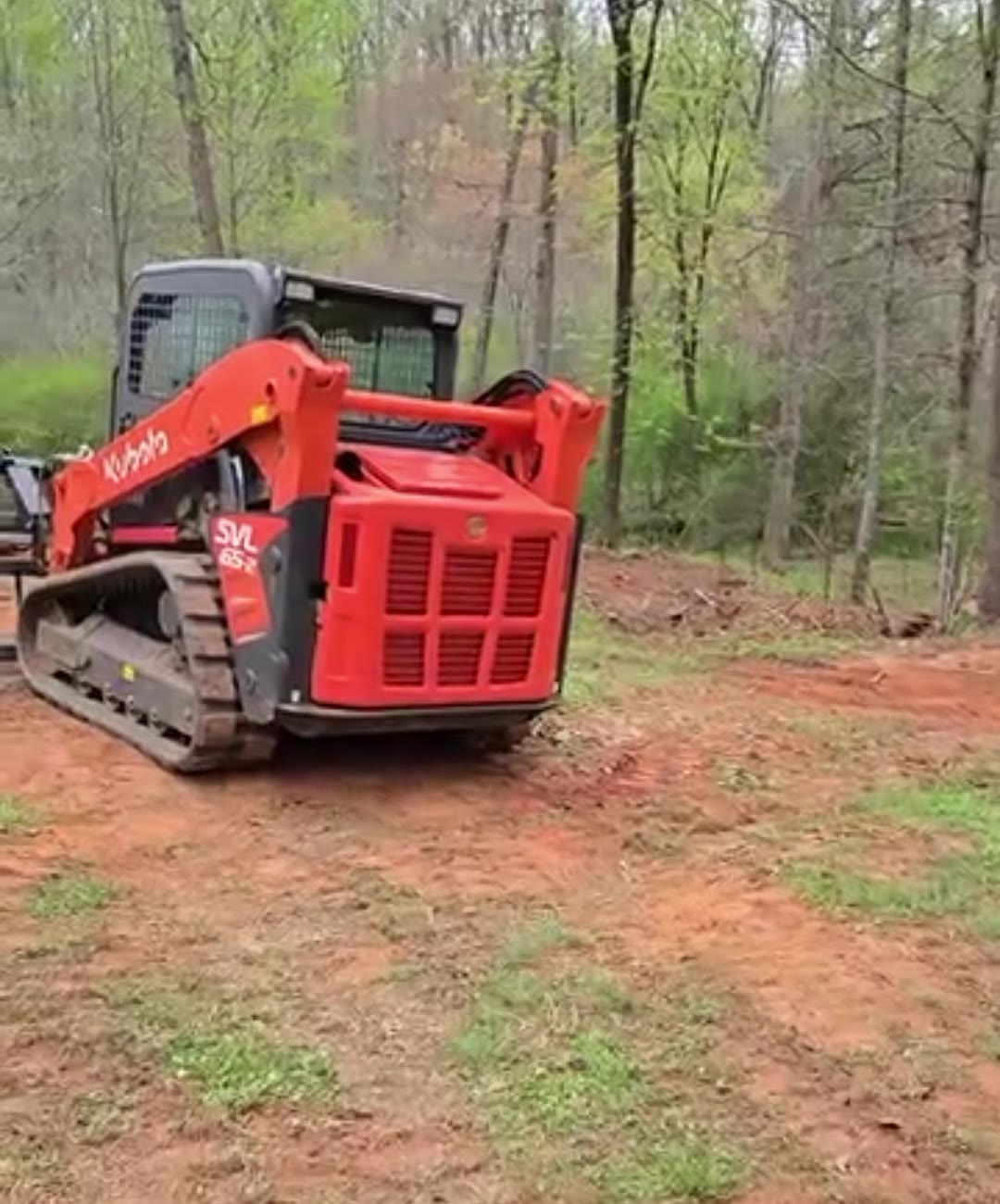 Orange Kubota track loader on a freshly cleared red-clay lot