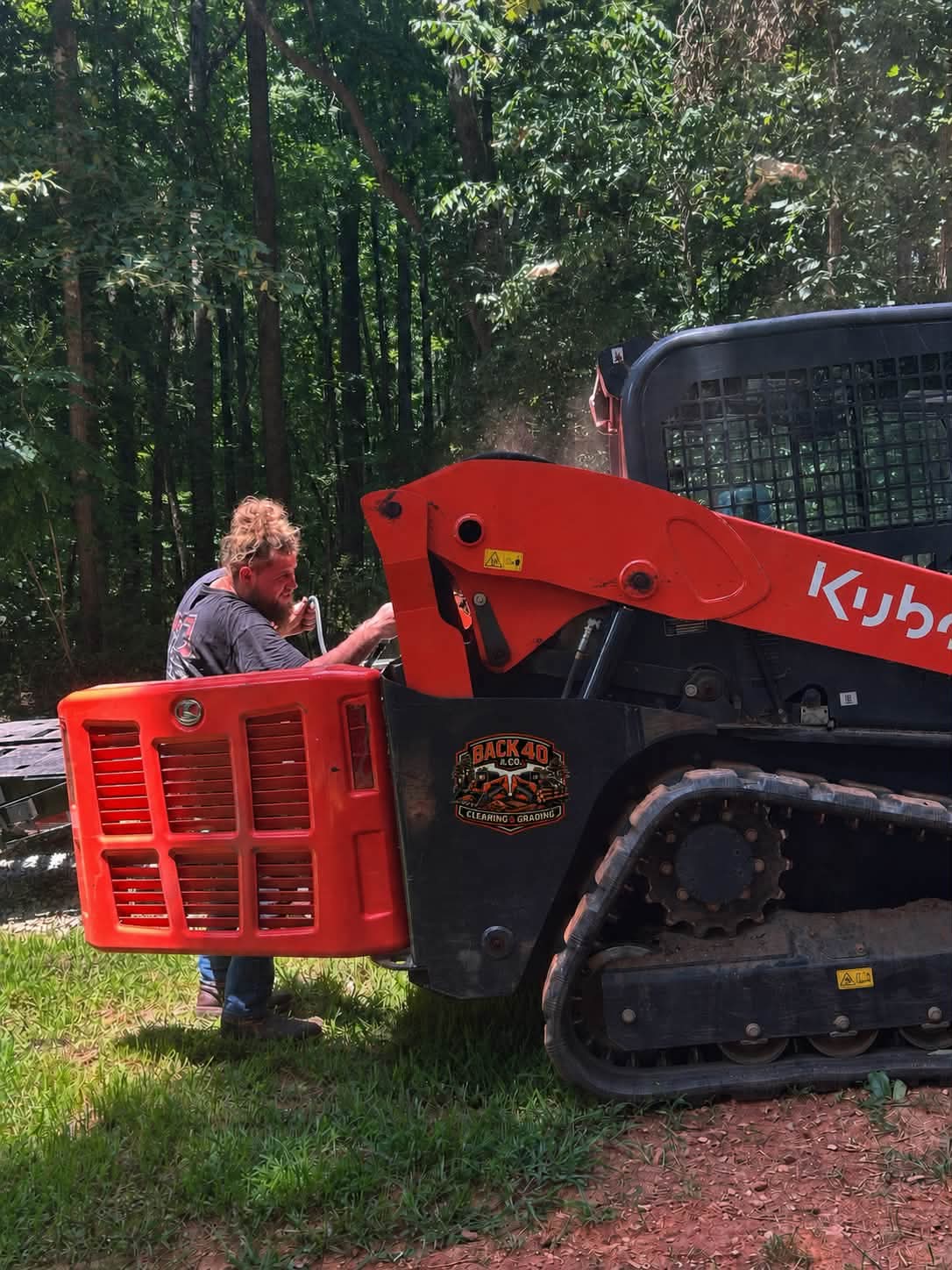 The orange Kubota track loader with the Back 40 logo sticker, getting serviced