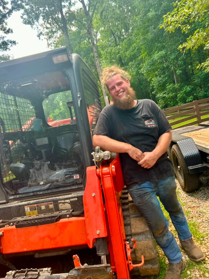 Smiling crew member leaning on the orange Kubota track loader, Digger Done