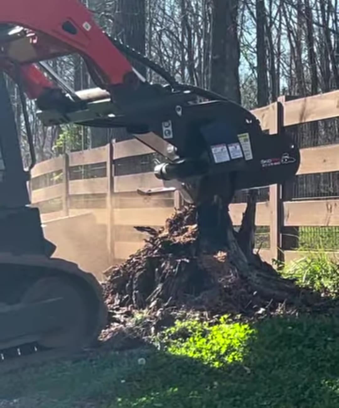 Stump grinder attachment chewing a stump down by a wooden fence